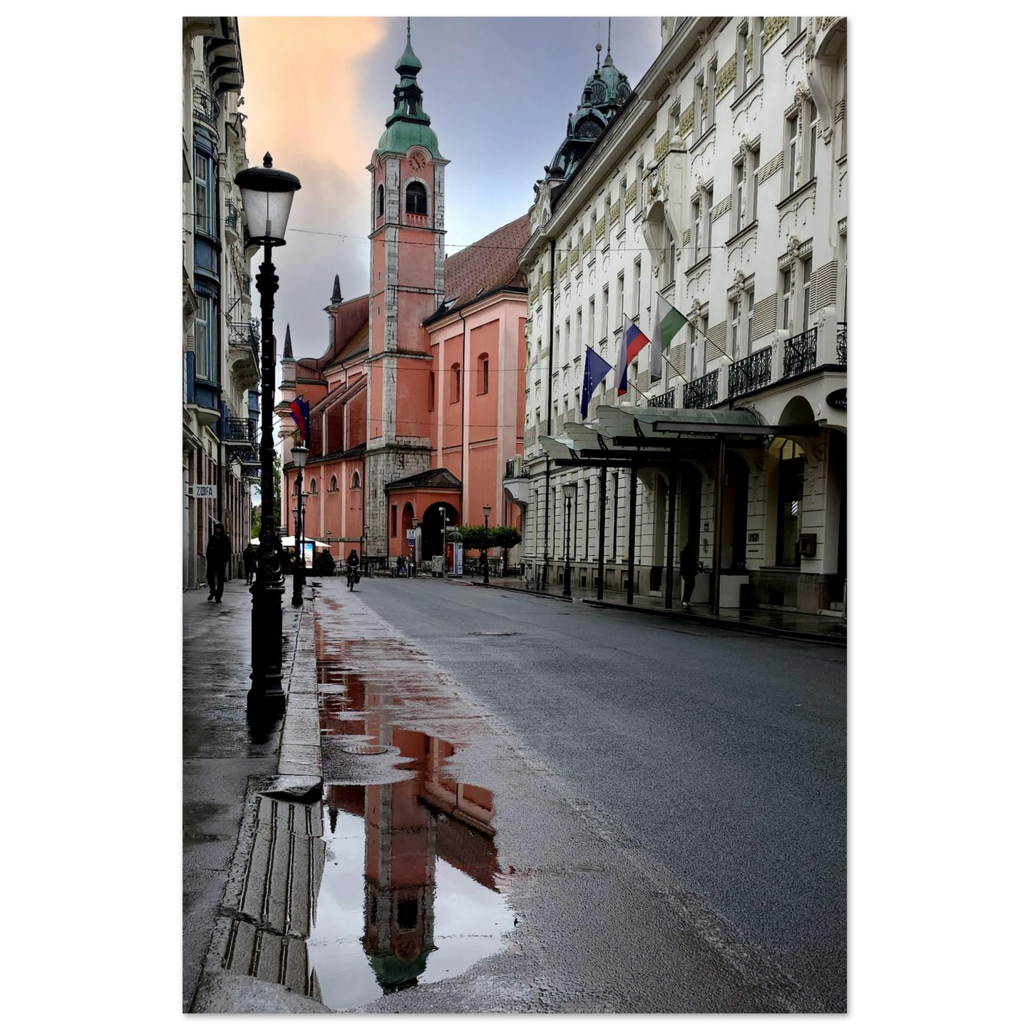 Photo par Kellestom. Cathédrale rose de Ljubljana reflétée dans une flaque d’eau sur une rue mouillée en Slovénie