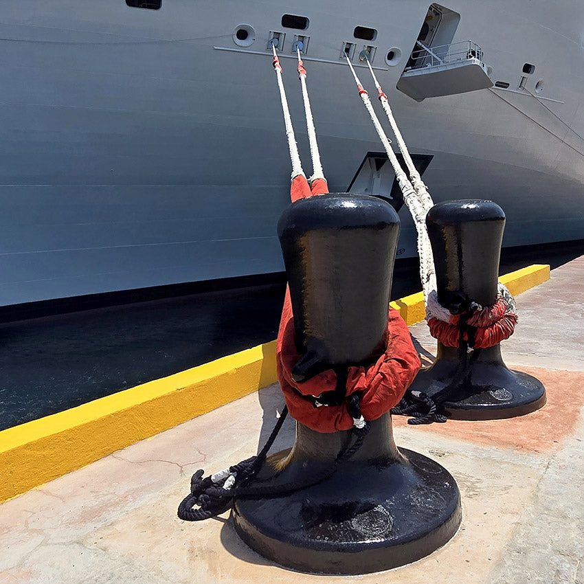 Deux bittes d'amarrage noires sur un quai portuaire tenant des aussières à fourreaux rouges reliées à un paquebot de croisière.