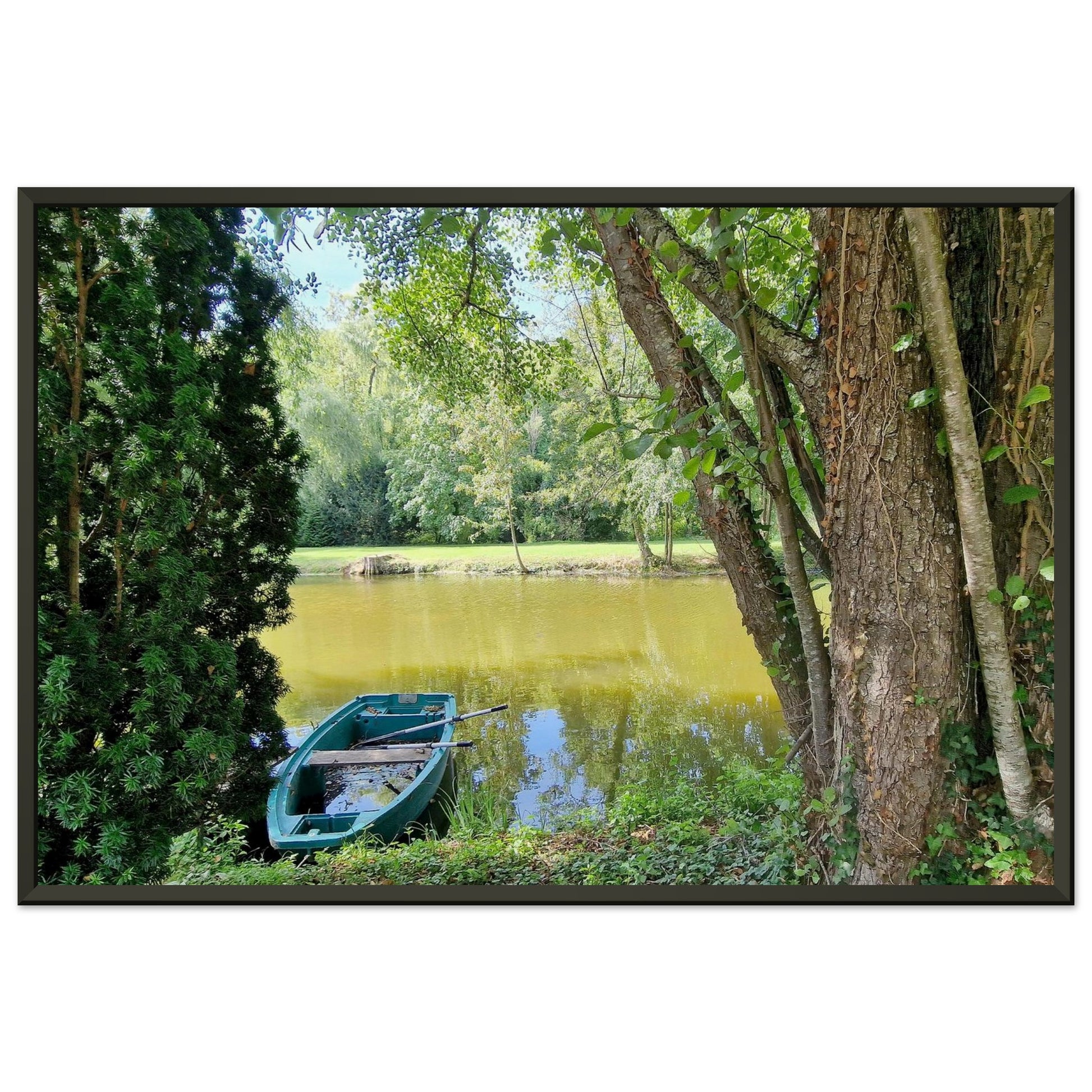 Petite barque en plastique bleu avec ses rames, amarrée au bord d'un étang paisible entouré d'arbres verdoyant