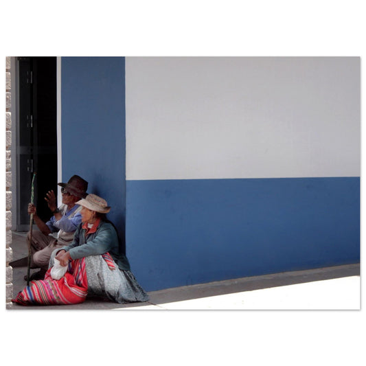 Photographie de deux personnes âgées en tenue traditionnelle péruvienne assises à l'ombre contre un mur bleu et blanc au Pérou