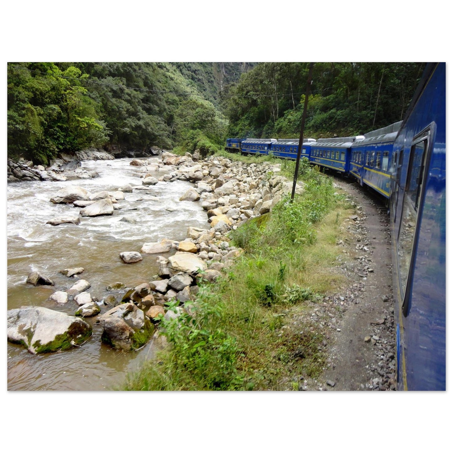 Photographie de voyage du train bleu PeruRail longeant la rivière Urubamba dans une vallée verdoyante des Andes vers le Machu Picchu - Collection Kellestom.