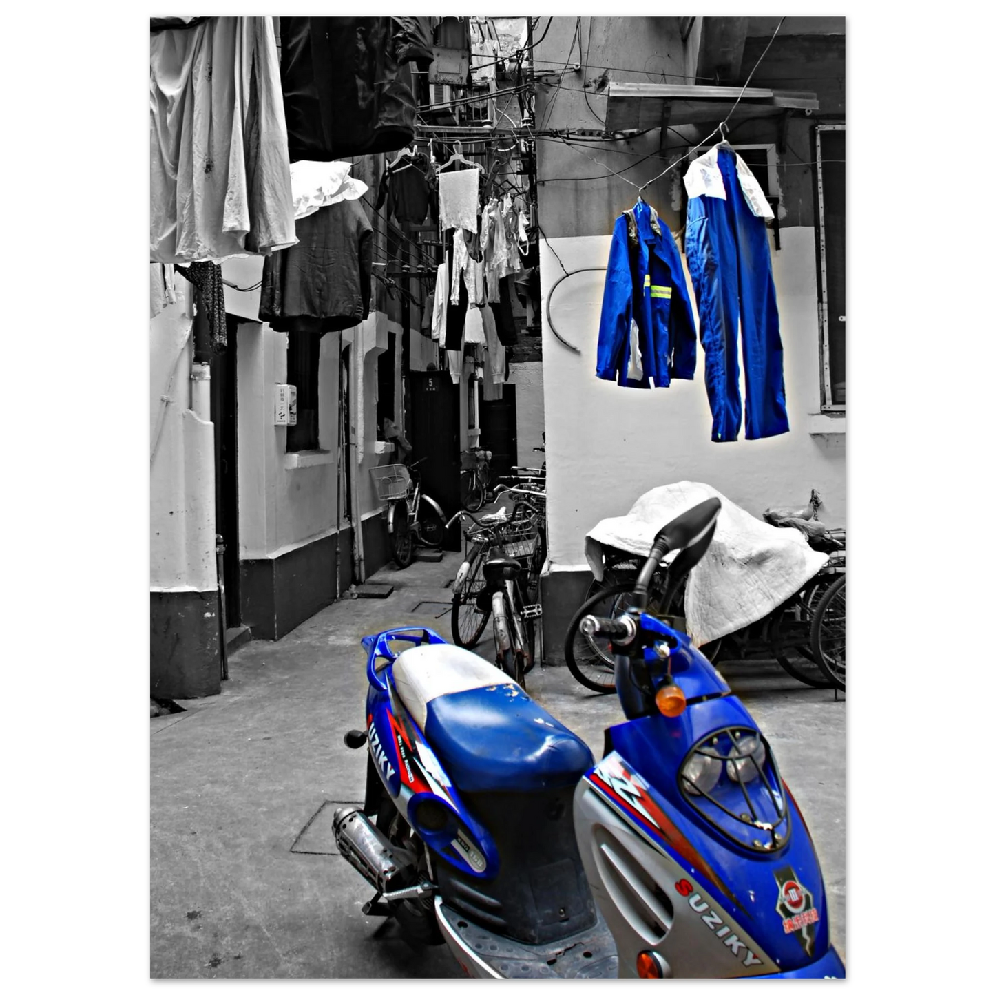 La photo en noir et blanc crée une ambiance nostalgique ou intemporelle, mettant en valeur les formes ,les textures de la moto et des vêtements suspendus.Shanghai moto suziky